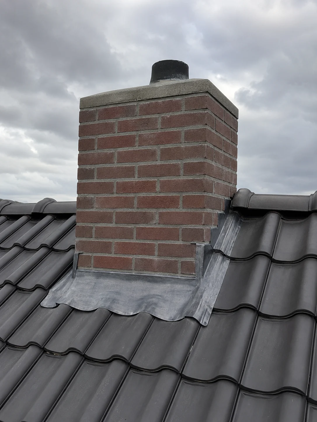 Illustratie bij schoorsteen-, lood- en zinkwerk: een gemetselde schoorsteen met loodwerk rondom de voet, van dichtbij.