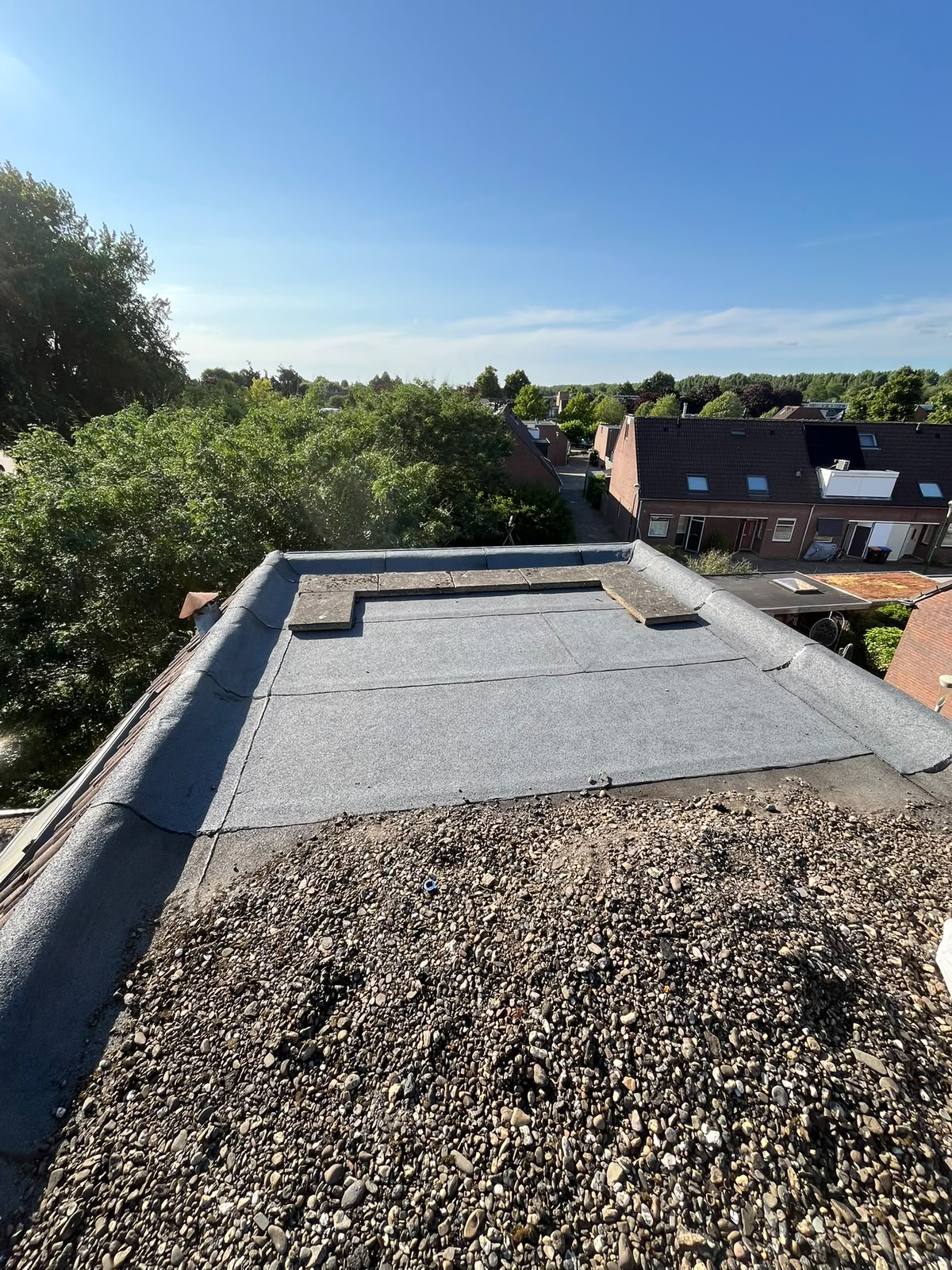 Plat dak met bitumen dakbedekking, afgewerkte randstroken langs de rand en een overgang naar een grindlaag op de voorgrond.