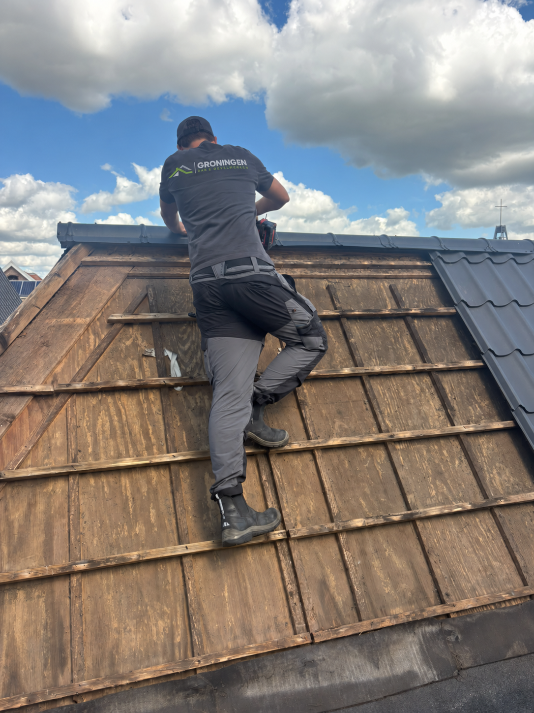 Vakman van Groningen Dak & Gevelwerken werkt aan de dakrand van een hellend dak, onder een bewolkte lucht.